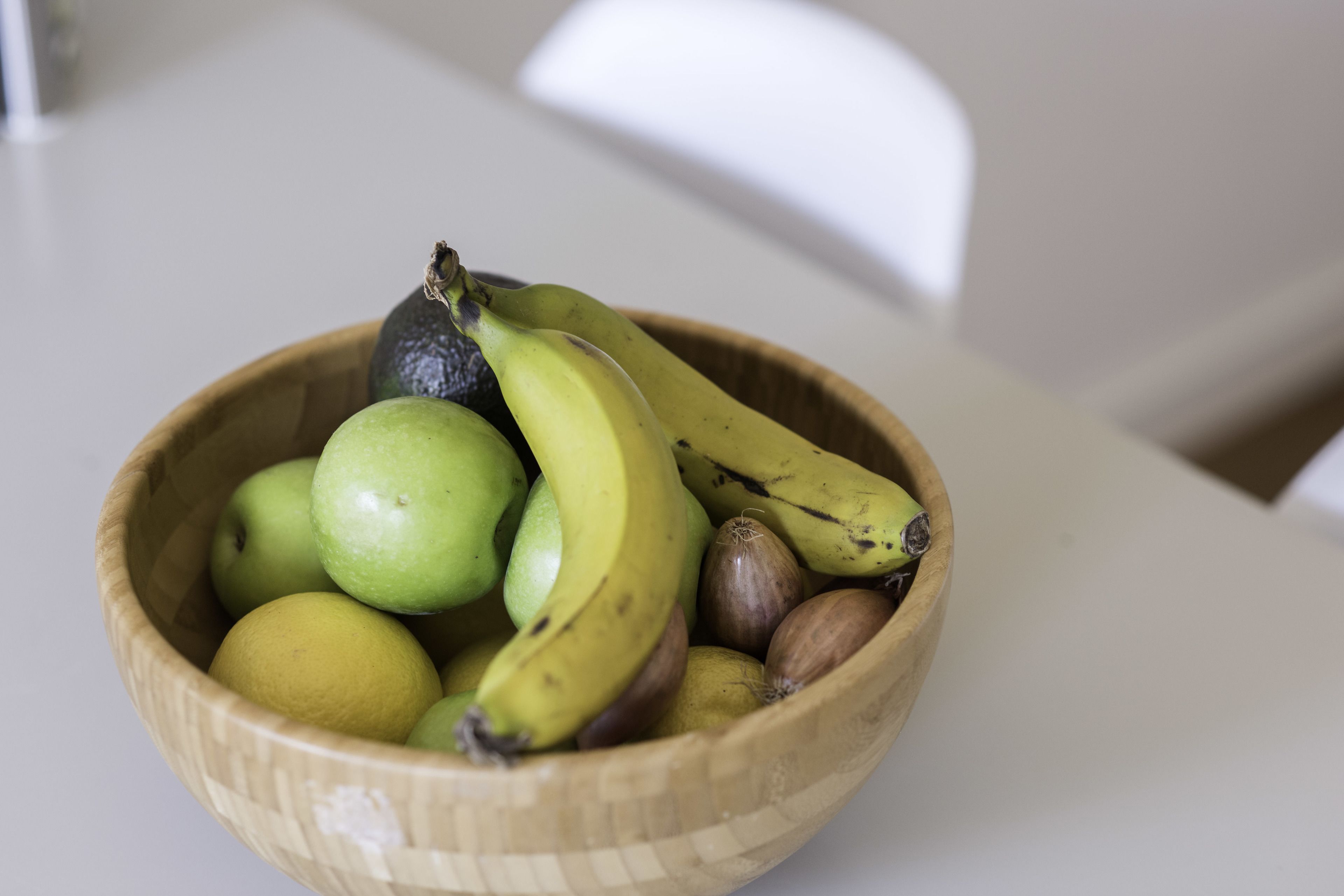 A wooden bowl containing green apples, bananas, and nuts on a table.