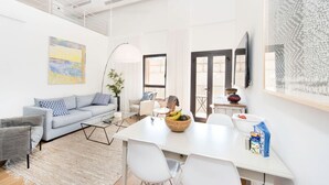 A modern living room with a grey sofa, white coffee table, and a dining area with a white table and chairs. - MAMAD - Jaffa Charm Seaview Stay by Sea N' Rent (Tel Aviv)