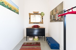 A room with a black dresser, a mirror with a decorative frame, a painting on the wall, a red and black cushion on the dresser, a blue storage box, and a red exercise bar. - MAMAD - Sea N'Rent - 204 Ben Yehuda Tel Aviv (Tel Aviv)