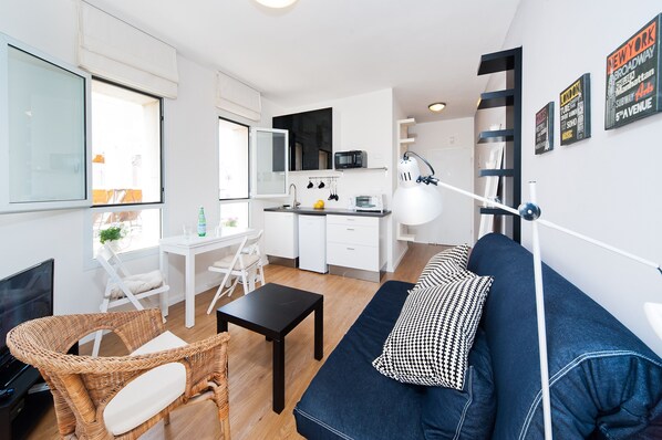 A modern apartment with a living room, dining area, and kitchenette. It features a sofa, a dining table, a TV, and a kitchenette with a microwave and toaster.