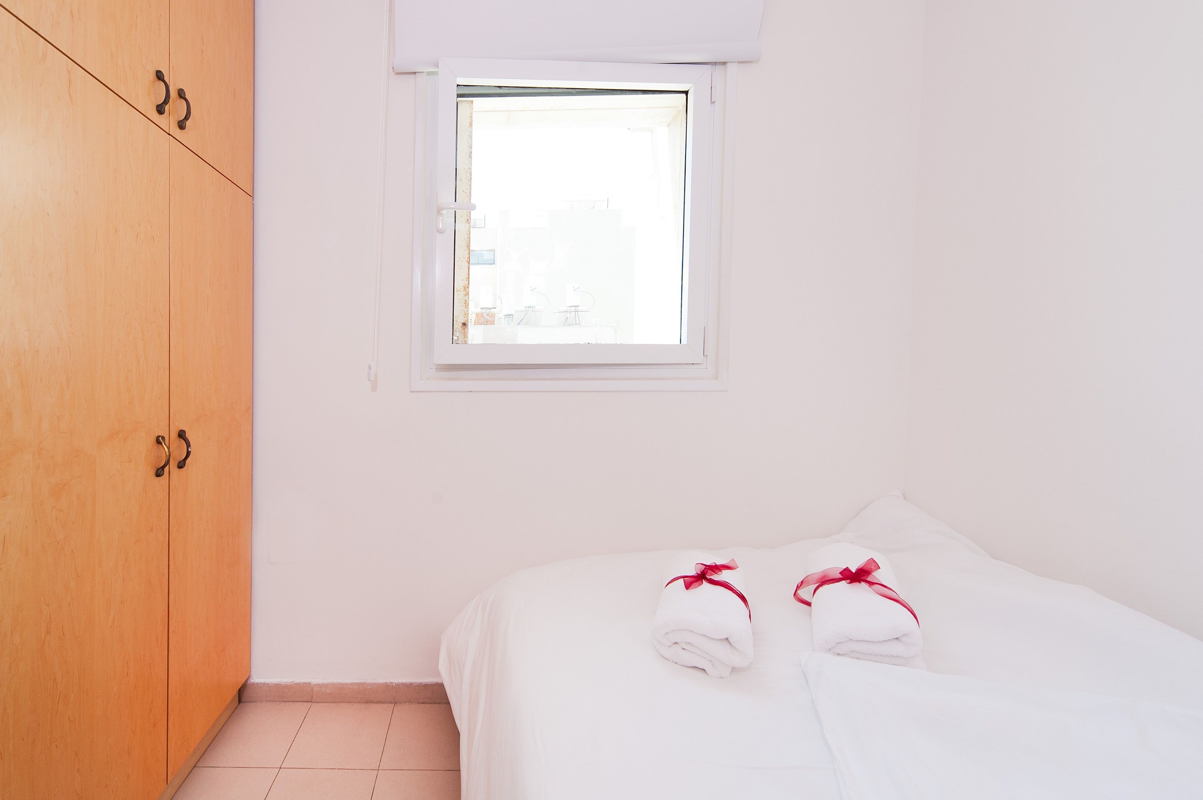 A bedroom with a wooden wardrobe, a window, and two towels on the bed.