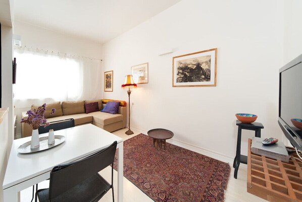 A modern living room with a white sofa, a dining table with chairs, a small round table, and a TV. - City Escape with Homey Vibes by Sea N Rent (Tel Aviv)