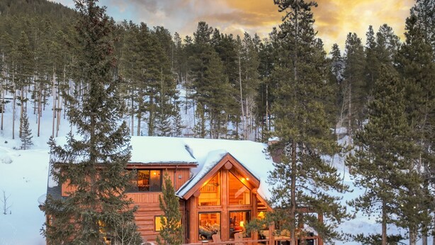 A wooden cabin with a balcony, surrounded by snow and trees.