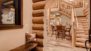 A log cabin interior with a wooden staircase leading to a dining area.