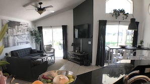 A modern kitchen with a black countertop, a dining area with a sofa and table, and a living room with a large window.