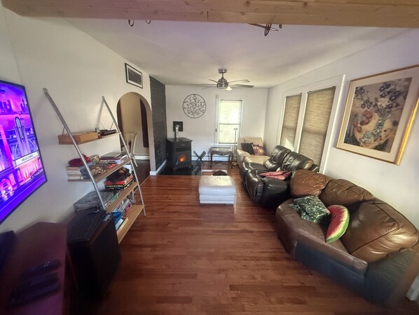 A cozy living room with a fireplace, leather sofa, wooden flooring, and a TV on the left.