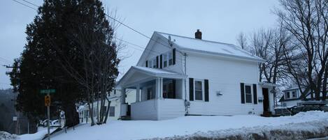 A two-story white house with a covered porch, surrounded by snow.