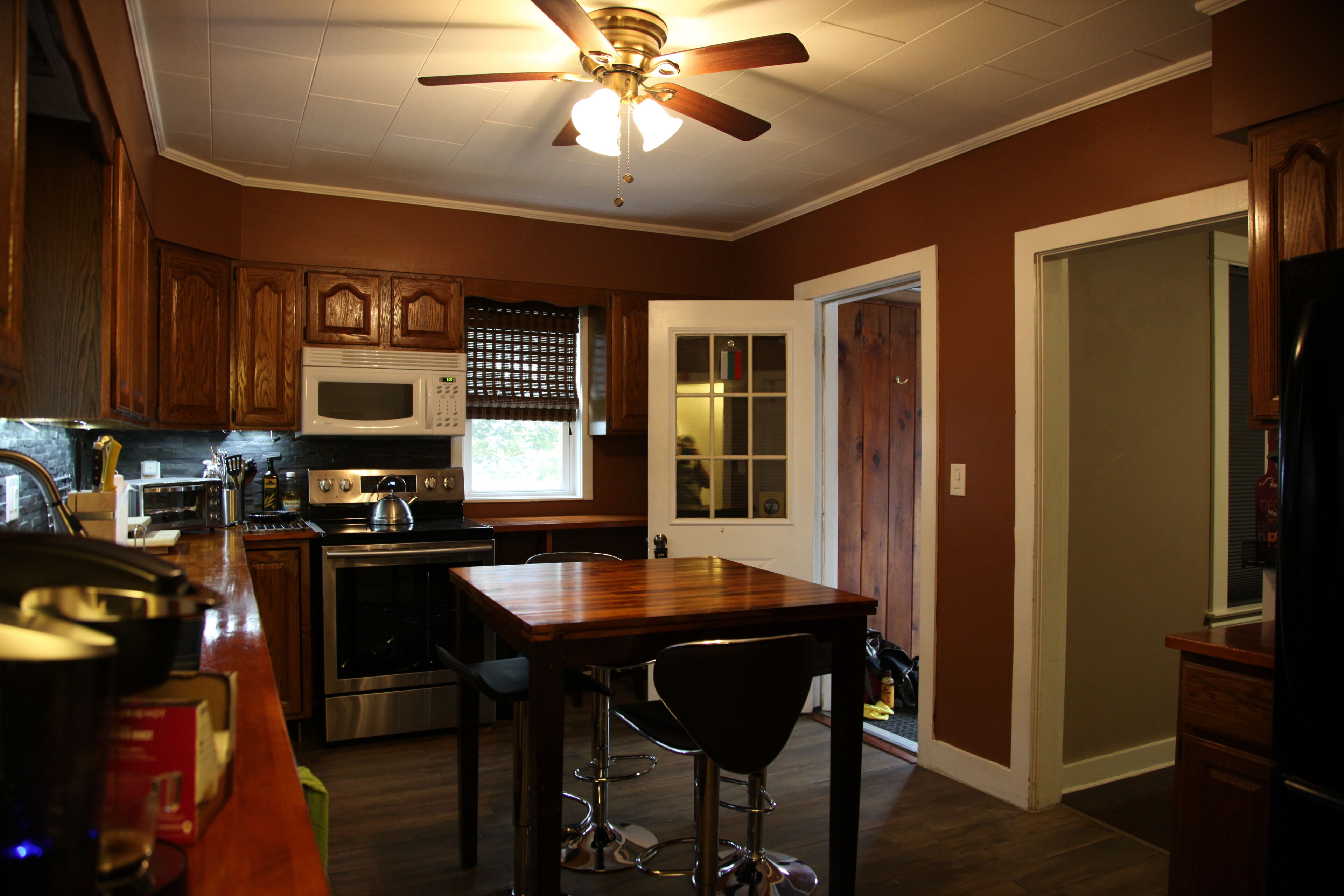 A kitchen with wooden cabinets, a microwave, an oven, and a dining table with bar stools.