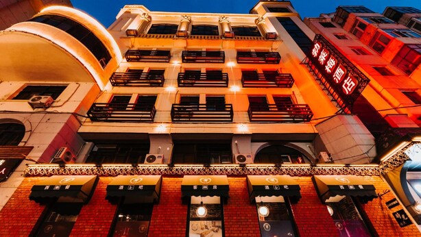 A multi-story building with a brick facade, multiple balconies, and illuminated signage. - Harbin Cloud Ma Bremei Inn Co Ltd (Harbin)