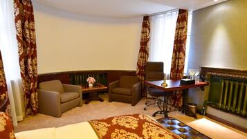 A hotel room with a bed, two armchairs, a small table with a vase of flowers, and a radiator.