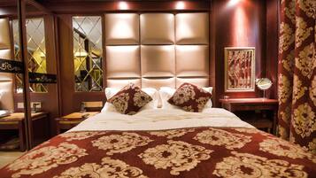 A hotel room with a large bed, a headboard with a light panel, a bedside table with a mirror, and a patterned carpet.