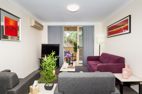 A modern living room with a grey sofa, a purple armchair, a coffee table, and a TV. There is a potted plant on the coffee table.