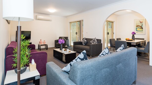 A modern living room with a sofa, armchair, and a coffee table. There is a TV, a lamp, and a small table with decorative items.