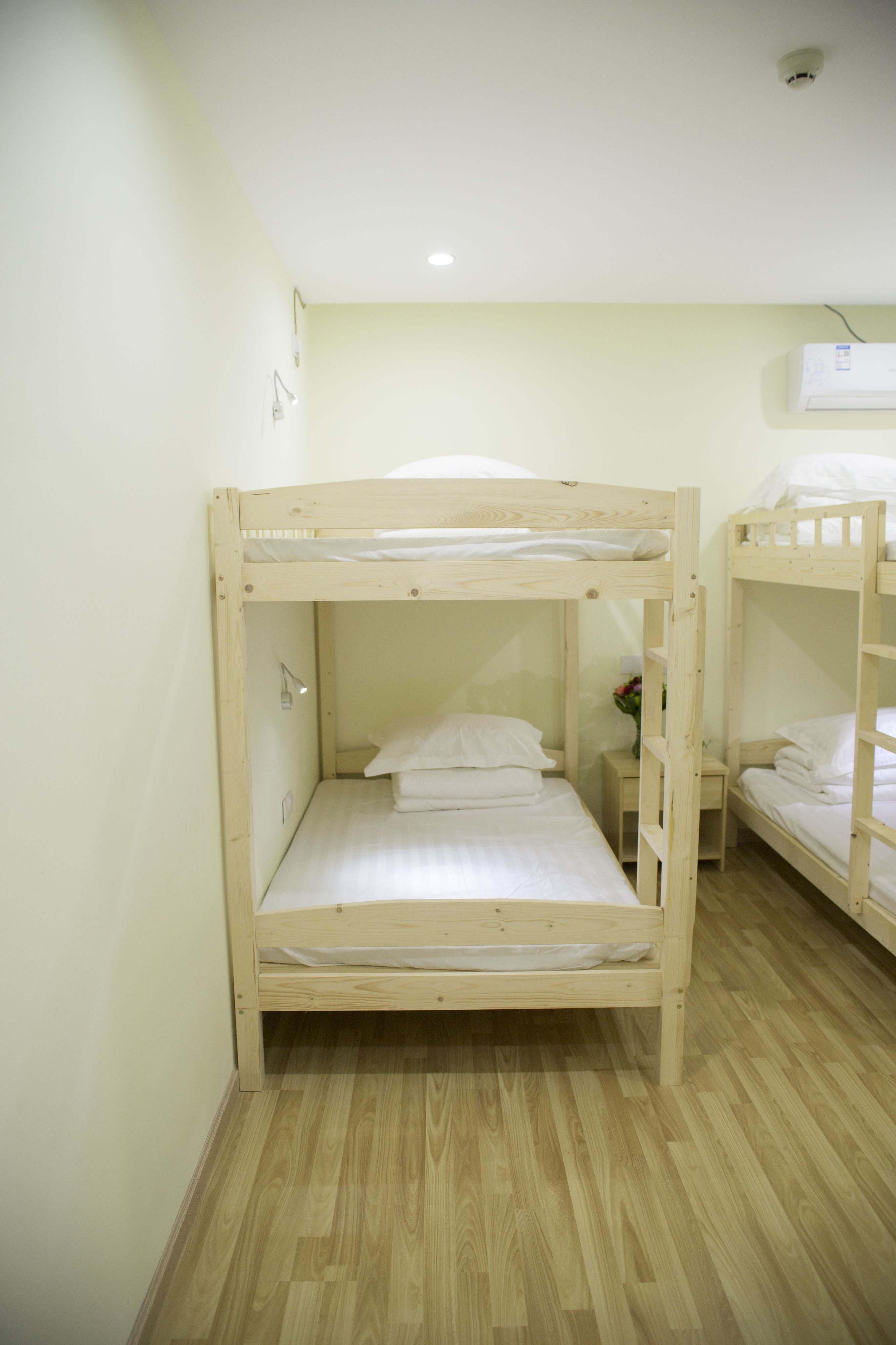 A bunk bed room with a wooden floor, a small bedside table, and a wall-mounted air conditioner.