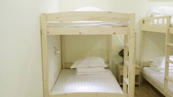 A bunk bed room with a wooden floor, a small bedside table, and a wall-mounted air conditioner.