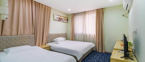 A hotel room with two beds, a desk with a computer, a wall-mounted air conditioner, and a window with curtains.