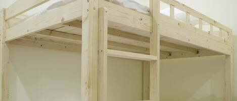A bunk bed with a wooden frame and white bedding, in a room with light-colored walls and wooden flooring.