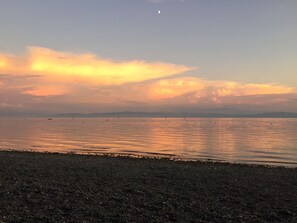 A beach with pebbles and calm water reflecting the sky.