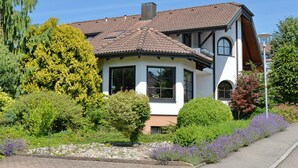 A two-story house with a tiled roof, surrounded by lush greenery and flowering plants. - Nice and quiet apartment in Markdorf am Gehrenberg with the Walther family (Markdorf)