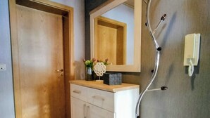 Um corredor com porta de madeira, armário branco, espelho e telefone fixado na parede.