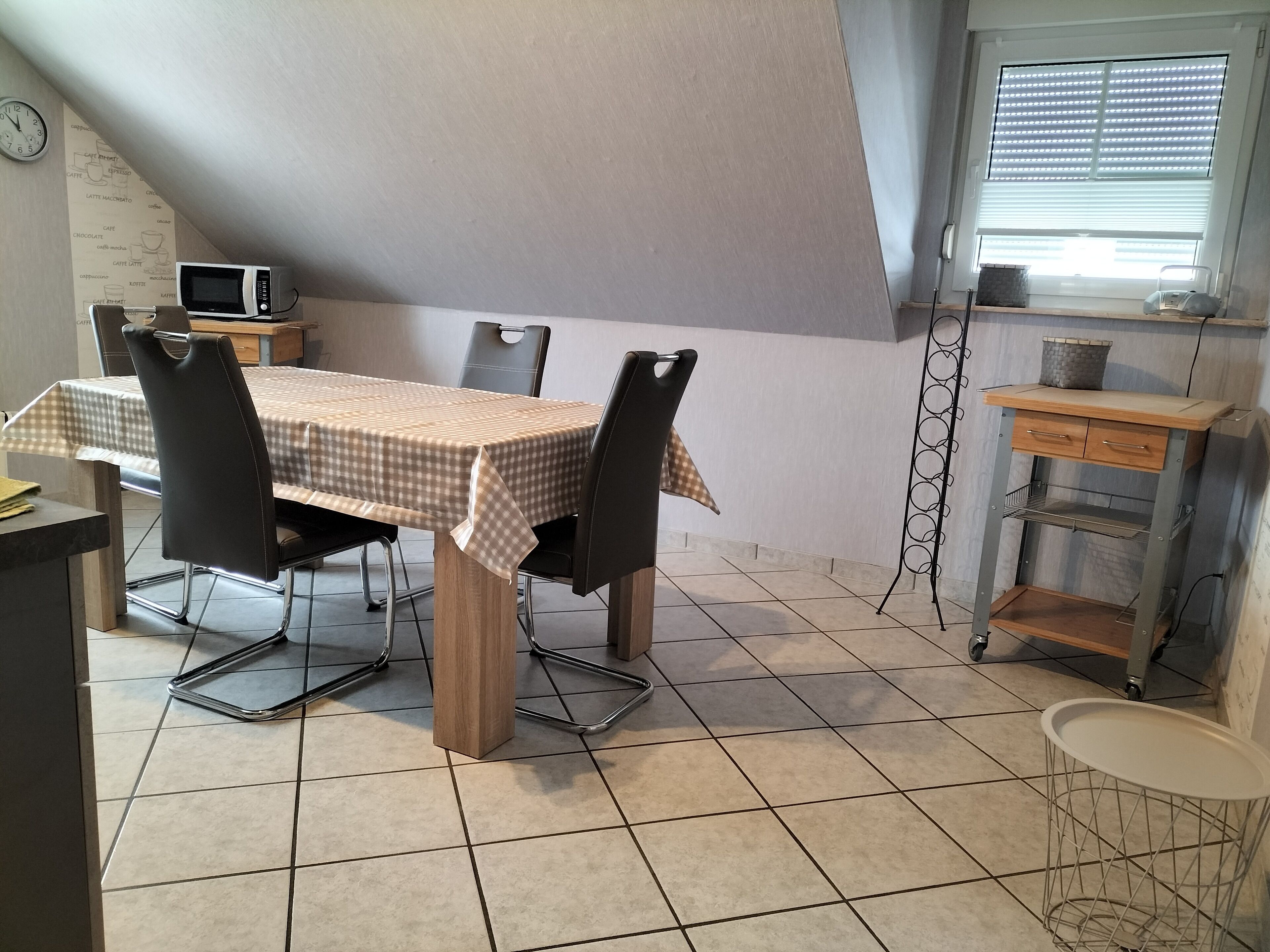 Un comedor con mantel a cuadros, sillas negras, un televisor pequeño y un mueble de metal.