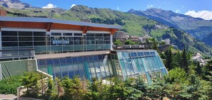 A modern building with large windows and a glass facade, set against a mountainous backdrop. - Spacious F3 South facing, Resort Center, Quiet, Terrace and Covered Parking  (Orcières)