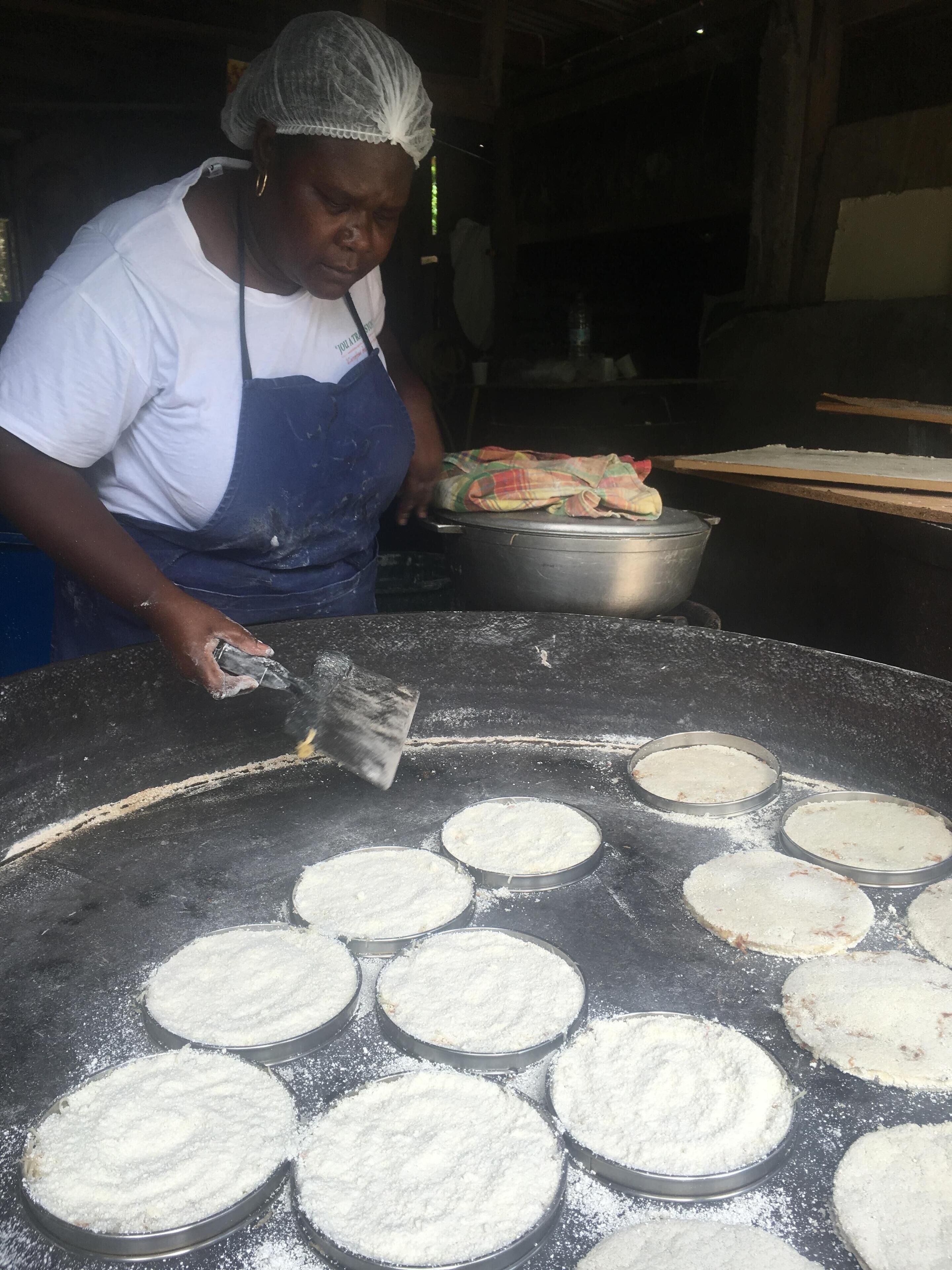 A person preparing food on a large griddle with multiple round pans.
