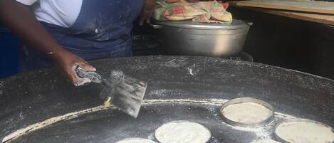 A person preparing food on a large griddle with multiple round pans.