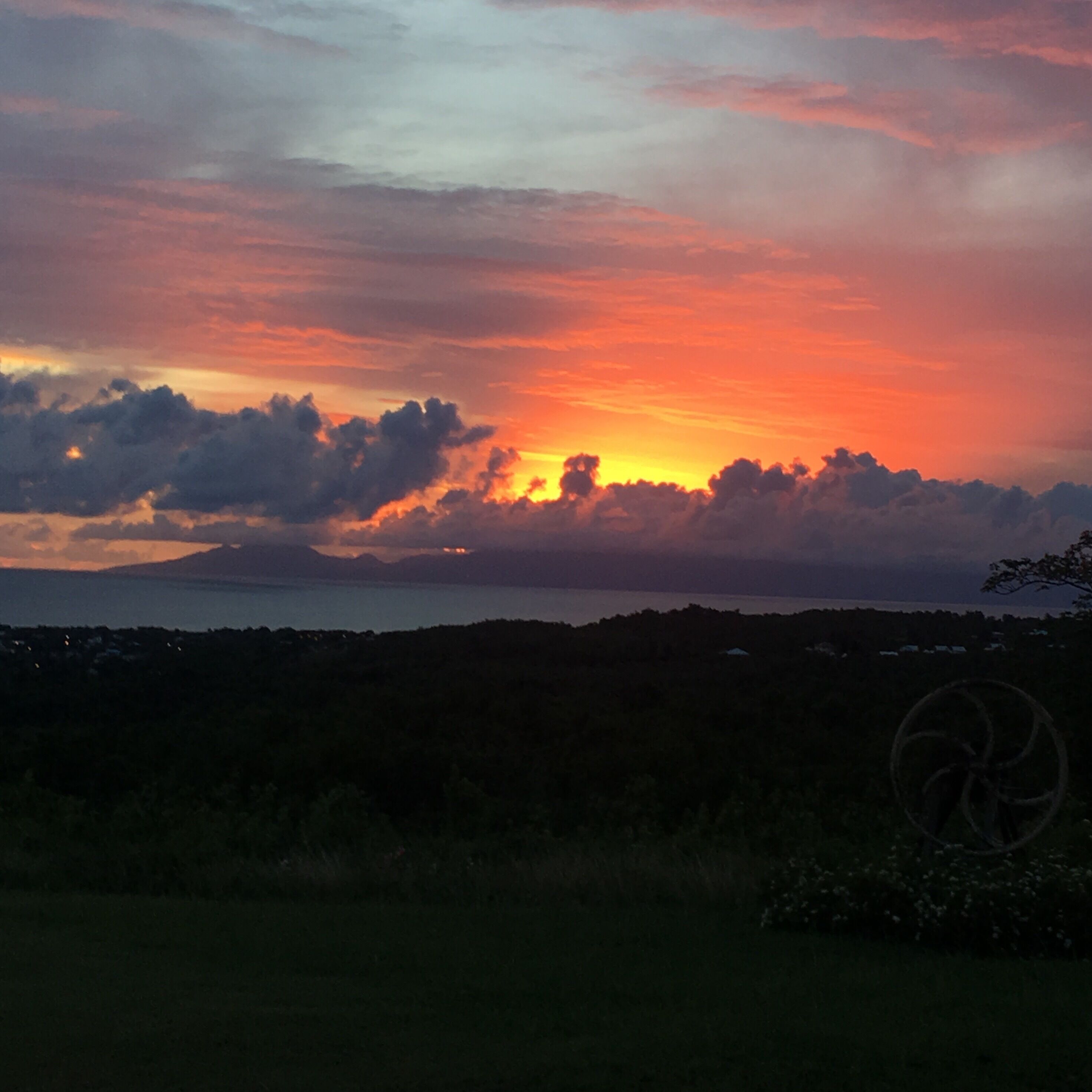 Um pôr do sol sobre uma paisagem costeira, com vista para o mar e colinas ao longe.