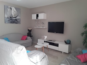Una sala moderna con un sofá gris, un armario blanco, una mesita blanca y un televisor de pantalla plana montado en la pared.