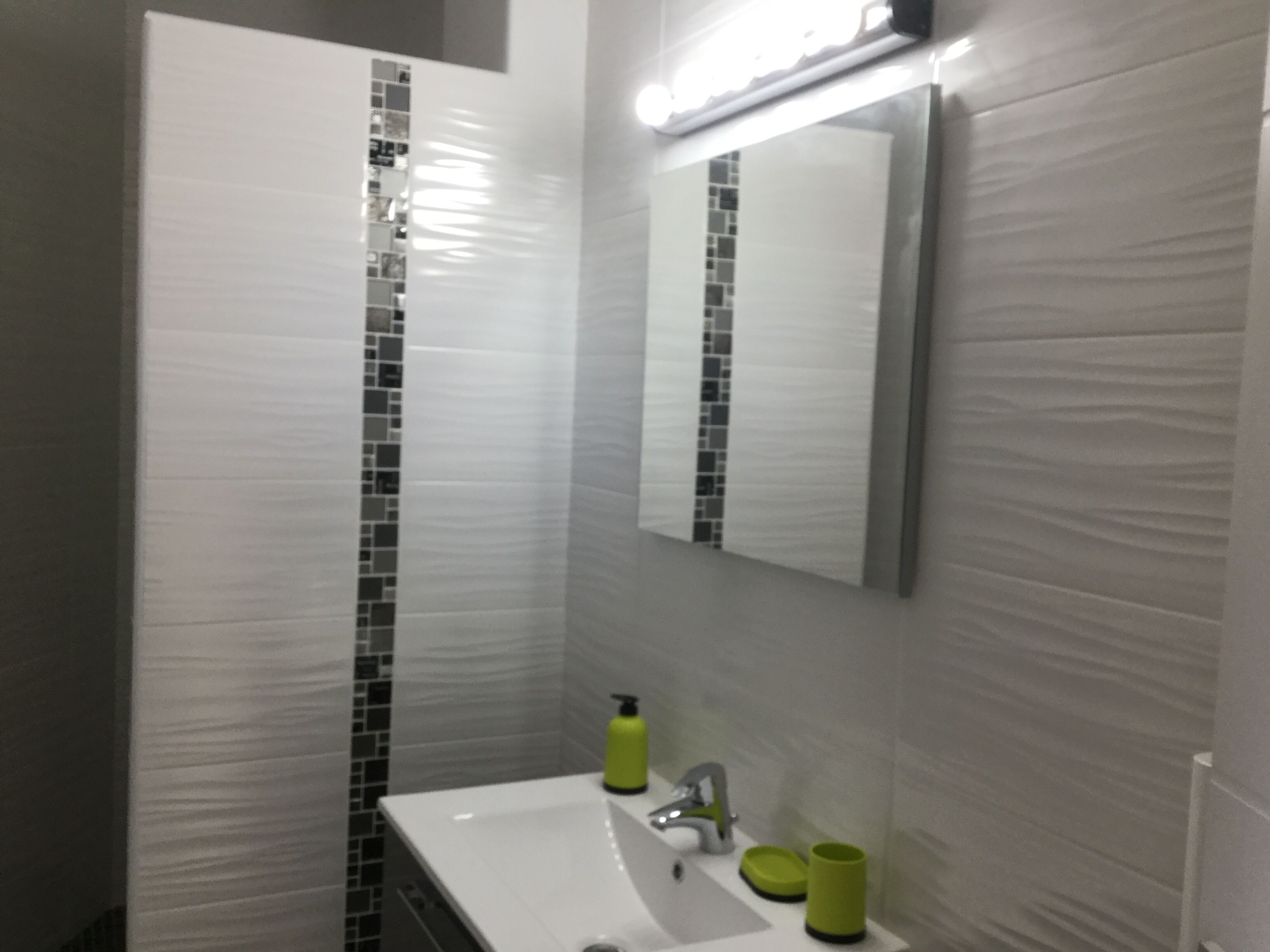 Un baño con un lavamanos blanco, un espejo y un dispensador de jabón verde.