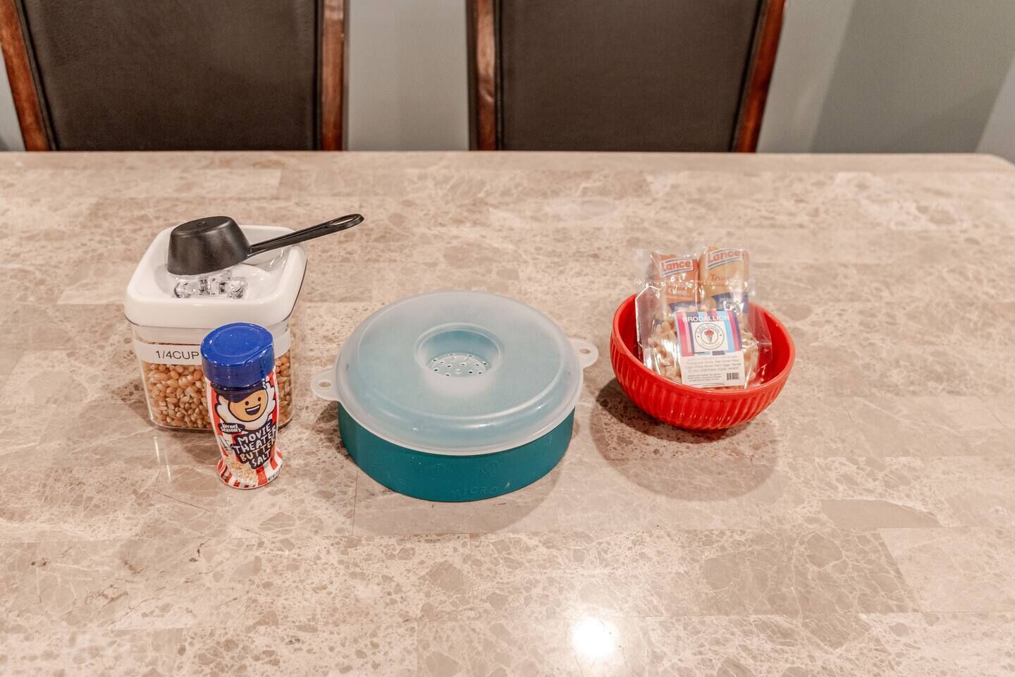 A kitchen counter with a food processor, a pot, a spice jar, and a red bowl with packaged items.