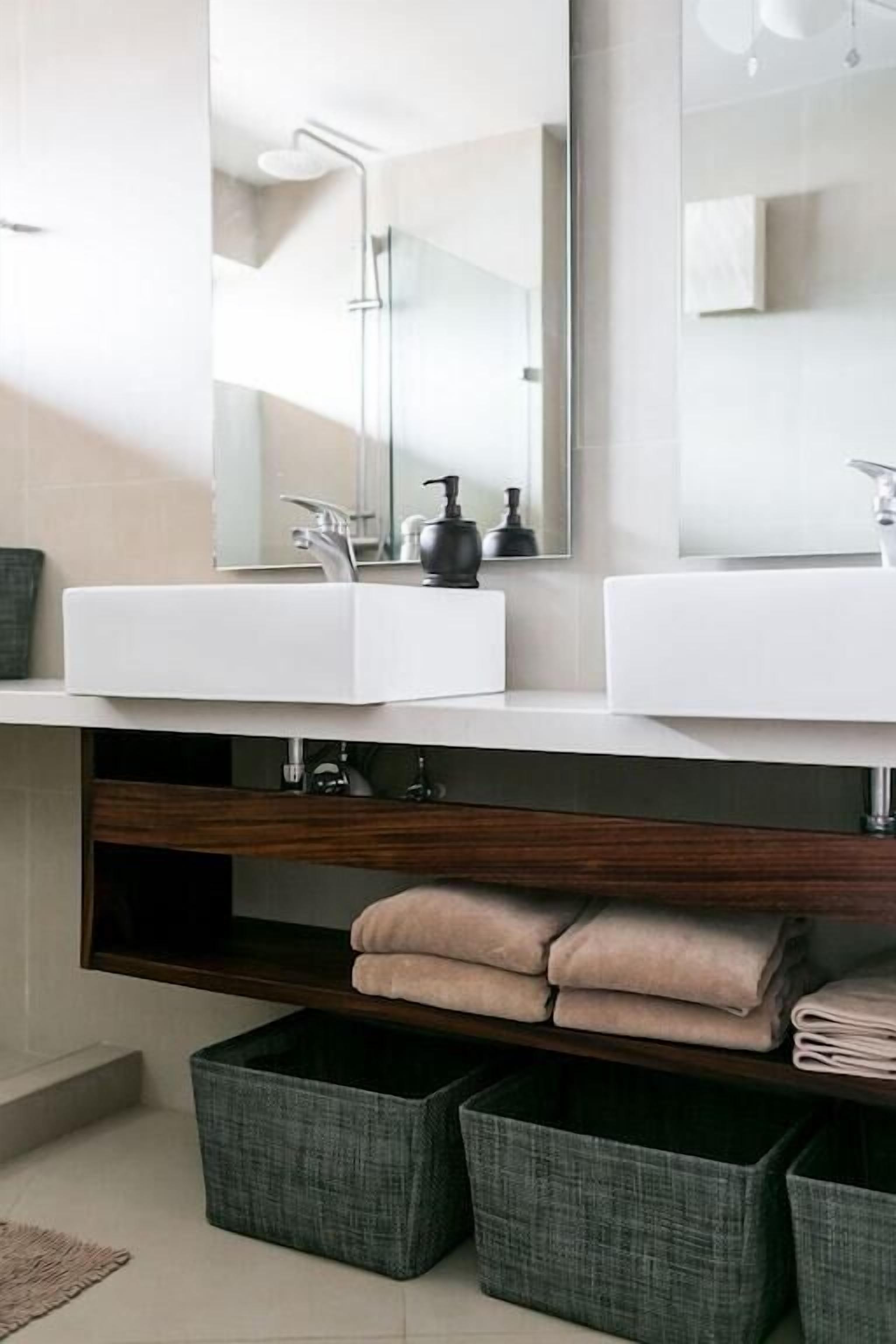 Een moderne badkamer met twee witte wasbakken, een grote spiegel en een houten plank eronder.