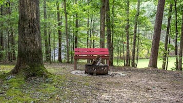 A forested area with a red bench and a metal fire pit.