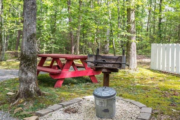 A picnic table and grill in a wooded area with a white picket fence. - Cozy/Convenient 2 PF Parkway/Screened In Porch (Sevierville)