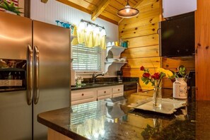 A kitchen with a stainless steel refrigerator, wooden wall paneling, a black countertop, and a sink.