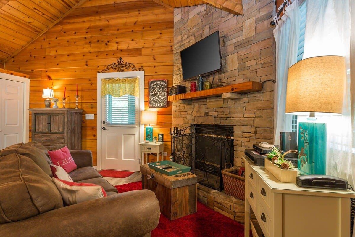 A cozy living room with a fireplace, wooden walls, a television mounted above it, and a comfortable sofa.