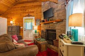 A cozy living room with a fireplace, wooden walls, a television mounted above it, and a comfortable sofa.