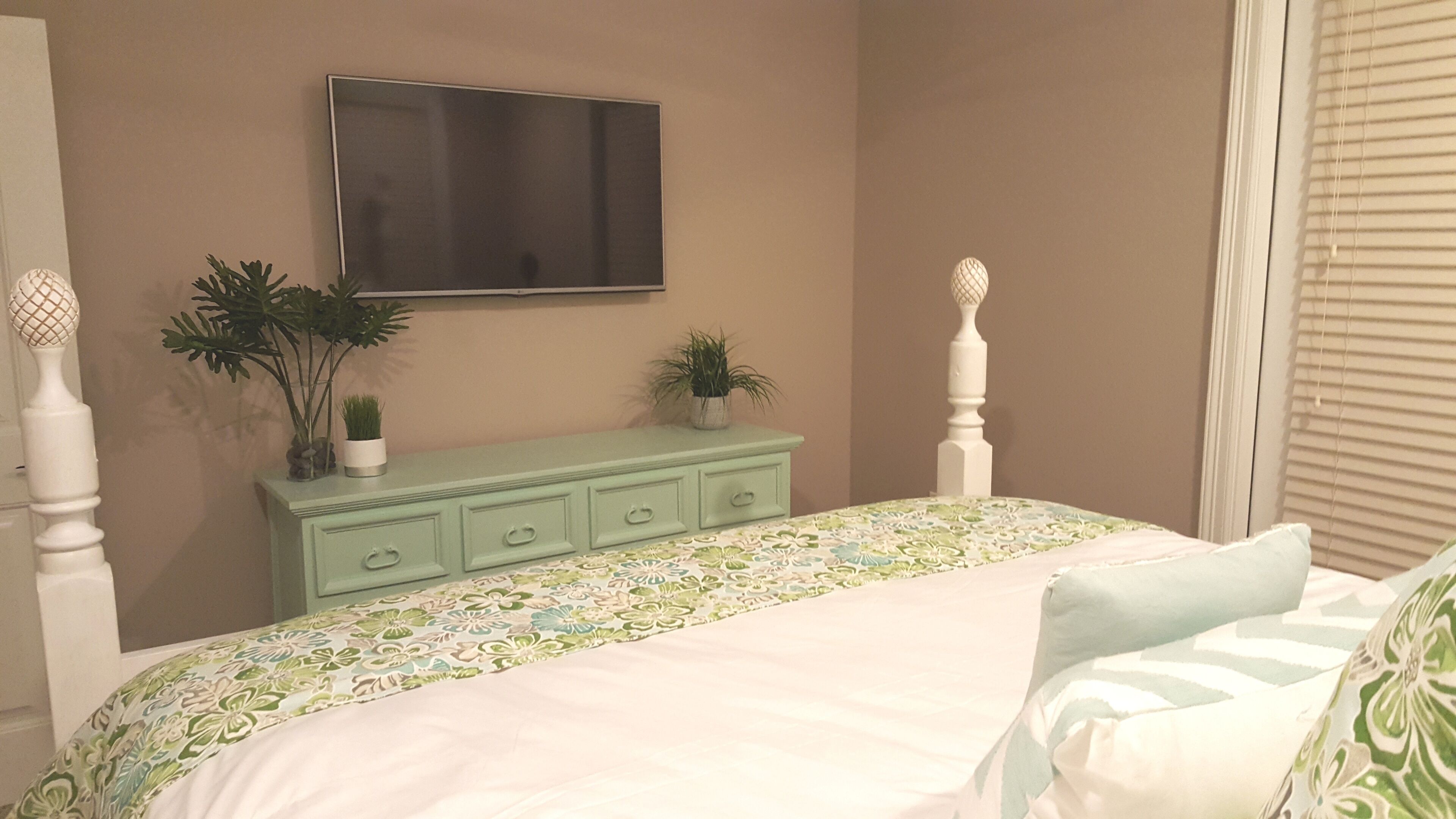 A bedroom with a bed, a dresser, and a TV mounted on the wall.