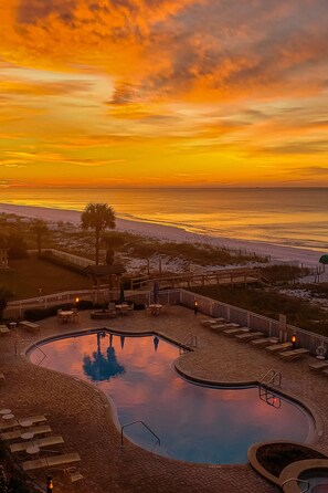 A pool area with a sunset view, wooden deck, and lounge chairs.