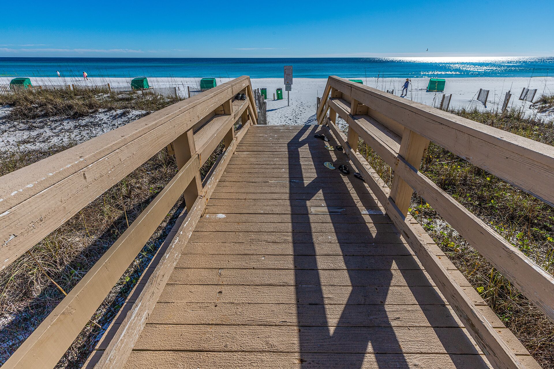 A wooden boardwalk leading to a beach with clear blue water and a sandy shore.