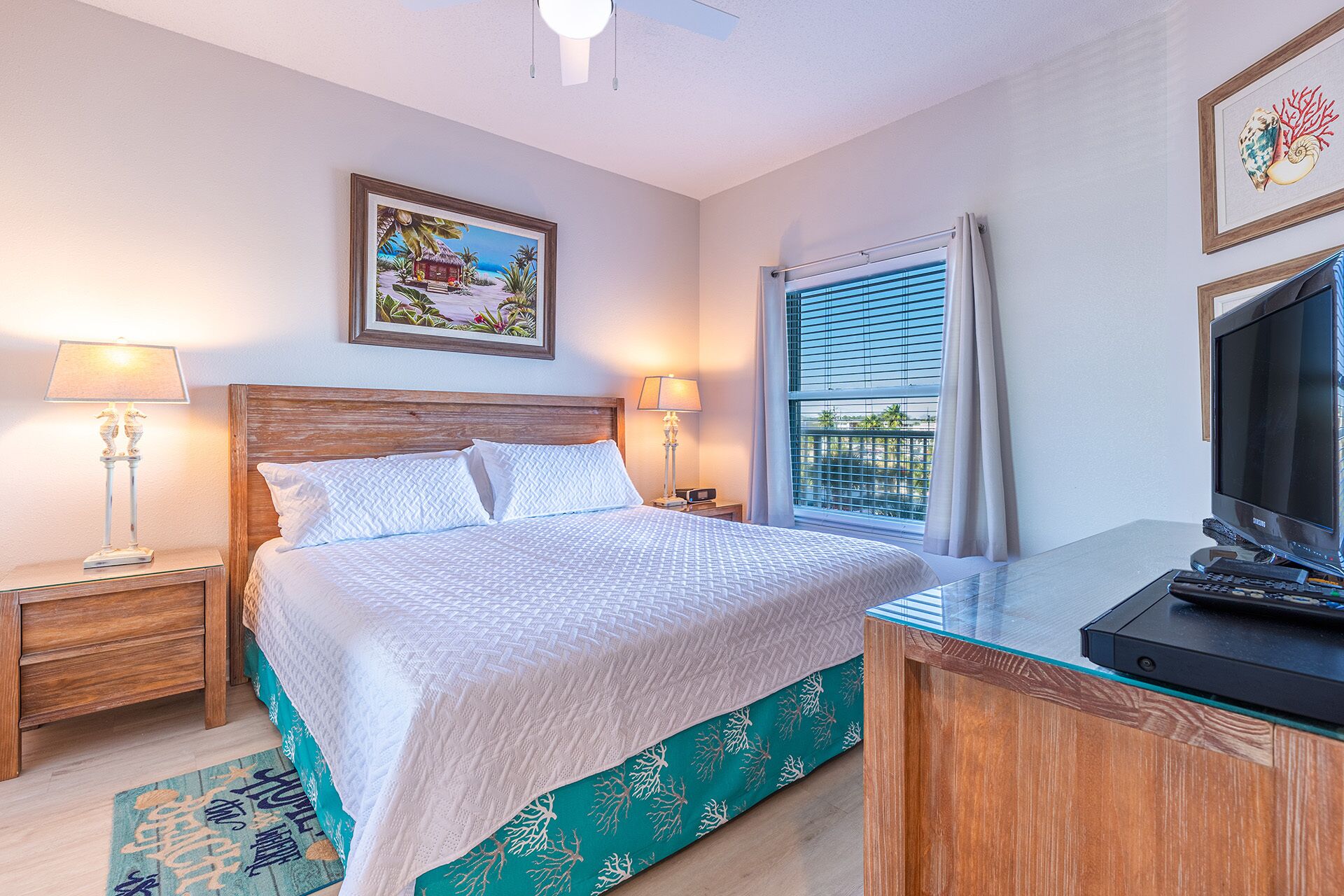 A hotel room with a bed, bedside lamps, a TV, a window with curtains, and a painting on the wall.