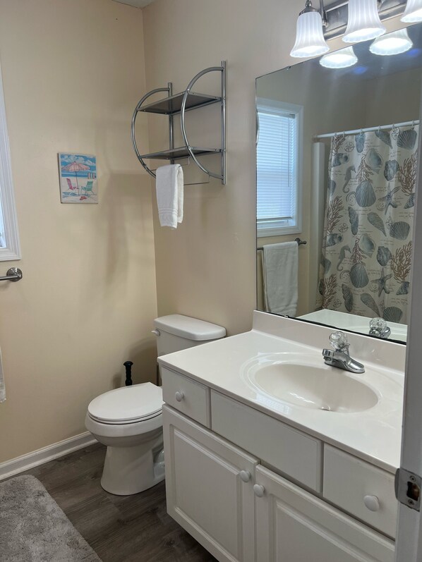 A bathroom with a toilet, a sink, a mirror, and a towel rack. - Reel Nice: 2nd Row Gem, Beach and Pier View from Balcony!  (Oak Island)
