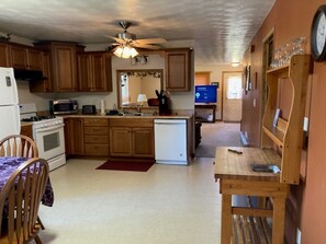 A compact kitchen with wooden cabinets, a microwave, a stove, and a small refrigerator. There is a dining table with chairs and a ceiling fan above.