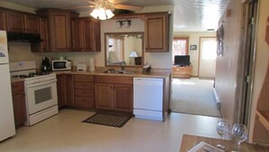 A kitchen with wooden cabinets, a microwave, a stove, and a ceiling fan. - Tin Mill Cottage on a quiet wooded lot, walking distance to downtown! (Hill City)