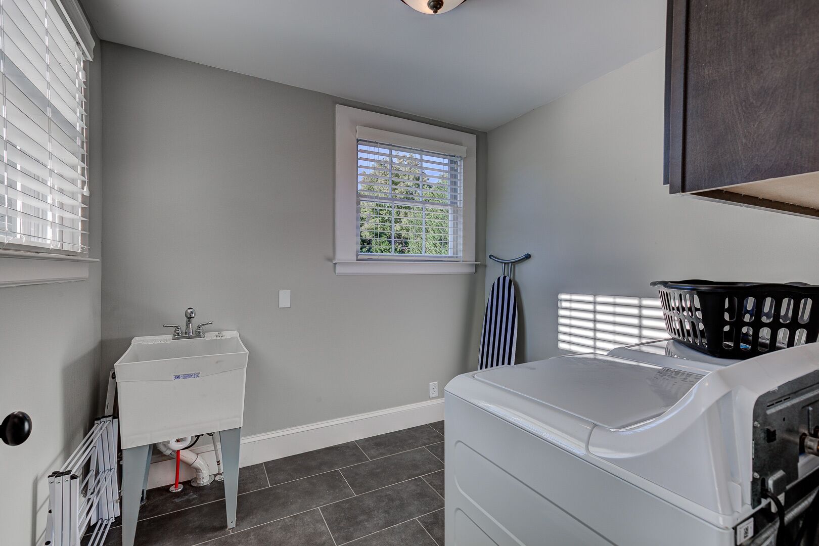 A laundry room with a washing machine, a sink, and a window with blinds.