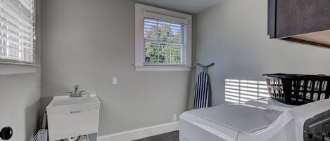 A laundry room with a washing machine, a sink, and a window with blinds.