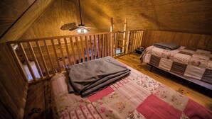 A cozy attic bedroom with a wooden ceiling, a bed with floral bedding, a quilted blanket, and a small table with a lamp. - Bass Cabin with hot tub (Fort payne)
