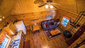 A wooden cabin interior with a dining area, sofa, and a ceiling fan. - Bass Cabin with hot tub (Fort payne)