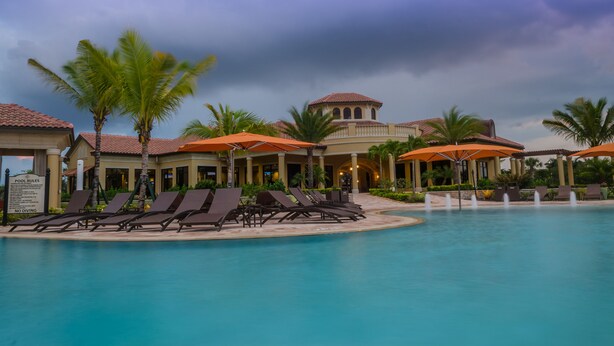 A pool area with lounge chairs and umbrellas, a sign indicating pool rules, and a building with a tiled roof. - January 2026 Still Available ! TREVISO BAY -RESORT. LUXURY POOL & Spa GOLF HOME (Naples)